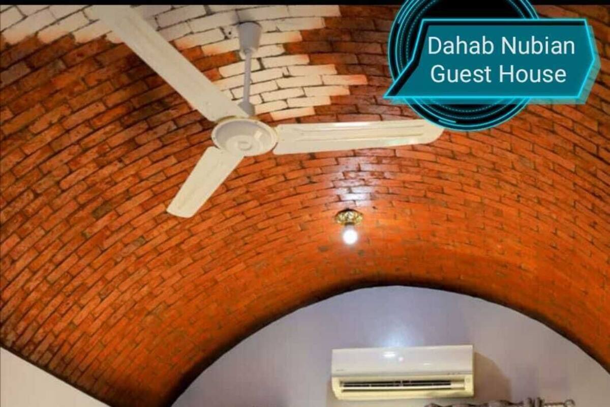 A guest room with a brick ceiling, an air conditioning unit, a bed with pillows, and a window with curtains.