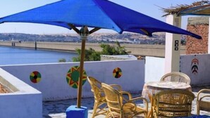 A rooftop terrace with a blue umbrella, wicker chairs, and a view of the sea. - Dahab Guest House (Aswan)