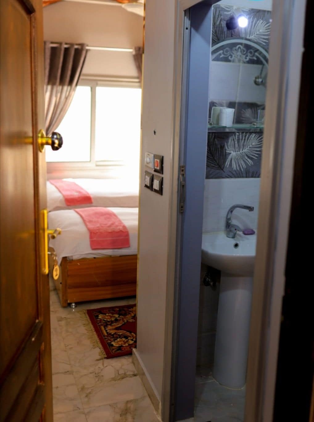 Una habitación de hotel con cama, baño con lavamanos y espejo, y ventana con cortinas.