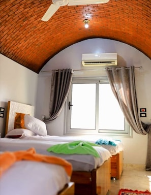 Una habitación de hotel con techo de ladrillo, unidad de aire acondicionado, cama con almohadas y ventana con cortinas.