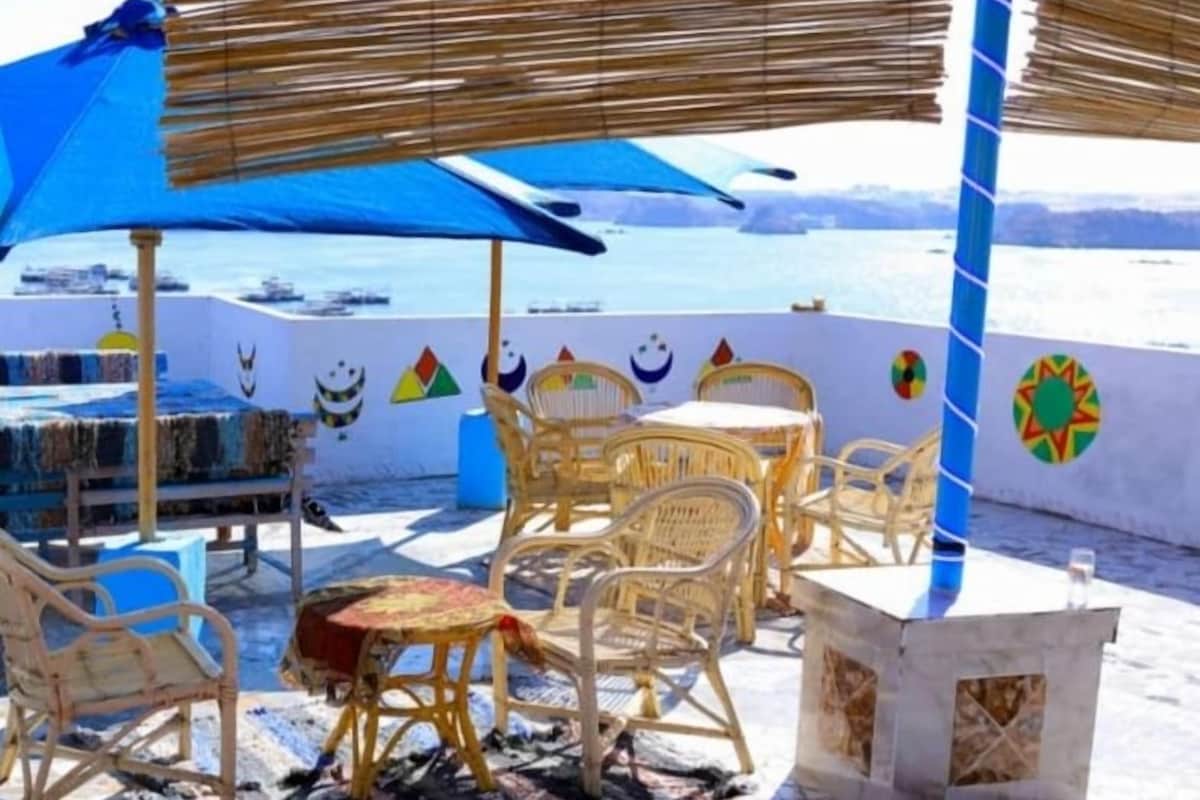 Una casa de huéspedes con asientos al aire libre, una sombrilla azul y vista al mar.