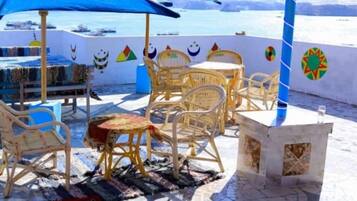 Una casa de huéspedes con asientos al aire libre, una sombrilla azul y vista al mar.