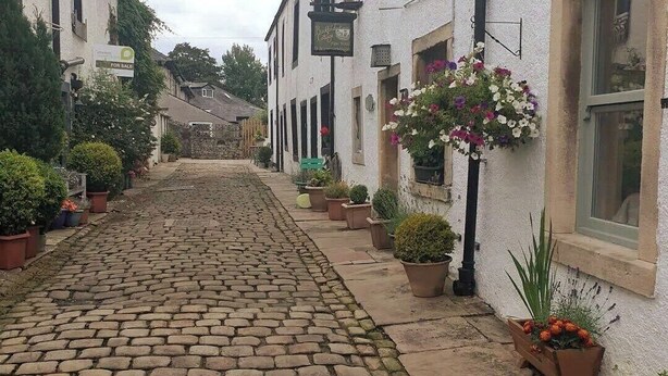 A cobblestone street lined with white buildings, some with signs indicating for sale.