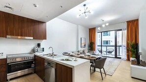 A modern kitchen with a central island, stainless steel appliances, and a dining area with a view to the outside. - Stylish 2BR in La Rive 2 (Dubai)