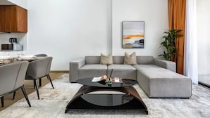 A modern living room with a grey sectional sofa, a round coffee table, and a dining area with a white table and chairs. - Stylish 2BR in La Rive 2 (Dubai)