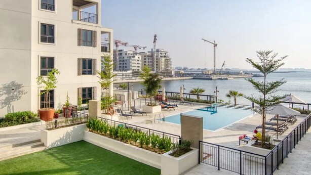 A rooftop pool area with a view of the sea, surrounded by modern buildings and construction cranes in the background. - Stylish 2BR in La Rive 2 (Dubai)
