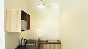 Una cocina compacta con un mueble de madera, un hervidor y un lavamanos.