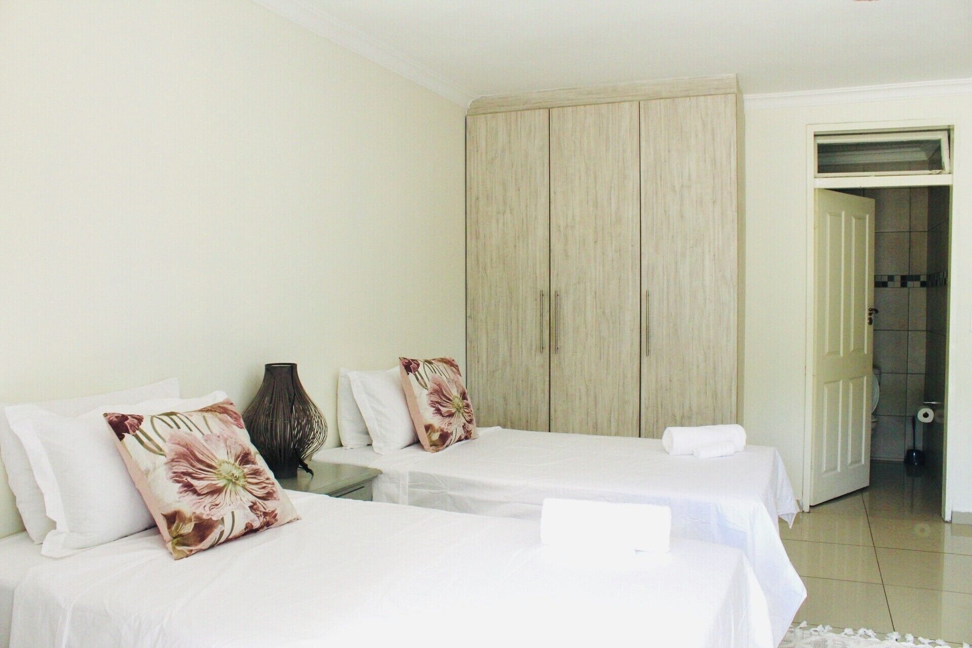A hotel room with two beds, a large wardrobe, and a bathroom visible through an open door.