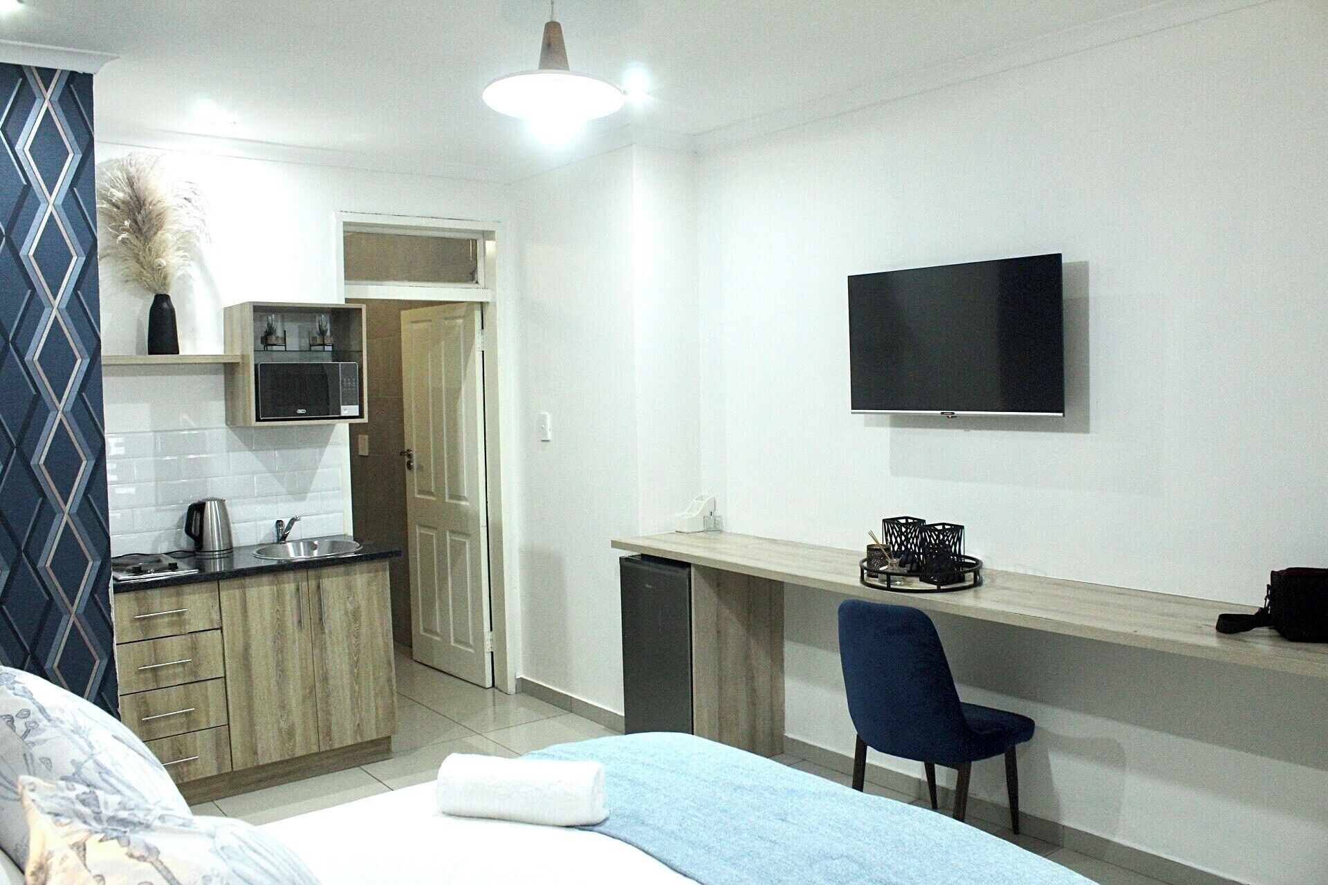 Habitación de hotel pequeña con cama, escritorio con silla, televisor, microondas y una kitchenette.