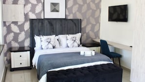 Une chambre à coucher comprenant un lit, une table de chevet, une chaise, un téléviseur et un mur orné d’un motif de plumes.