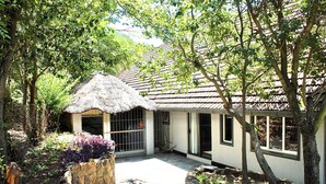 Une maison au toit de chaume, entourée d’arbres et d’un jardin.