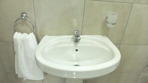 A bathroom with a white sink, a towel hanging on a metal ring, and a soap dispenser on the wall.