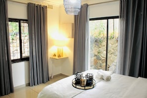 A hotel room with a bed, a bedside lamp, a tray with towels, and a view of greenery through the window. - Stunnning 1-bed Apartment in Sandton (Johannesburg)