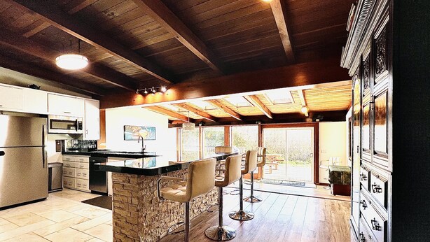 A modern kitchen with a stone island, bar stools, and a large window.