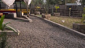 Un sendero de grava con borde de piedra, una valla de madera y una zona cubierta con un banco.