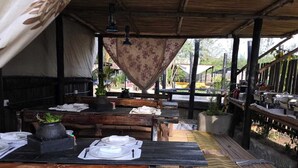 Un área de comedor al aire libre con mesas y bancos de madera, cubierta por un toldo.