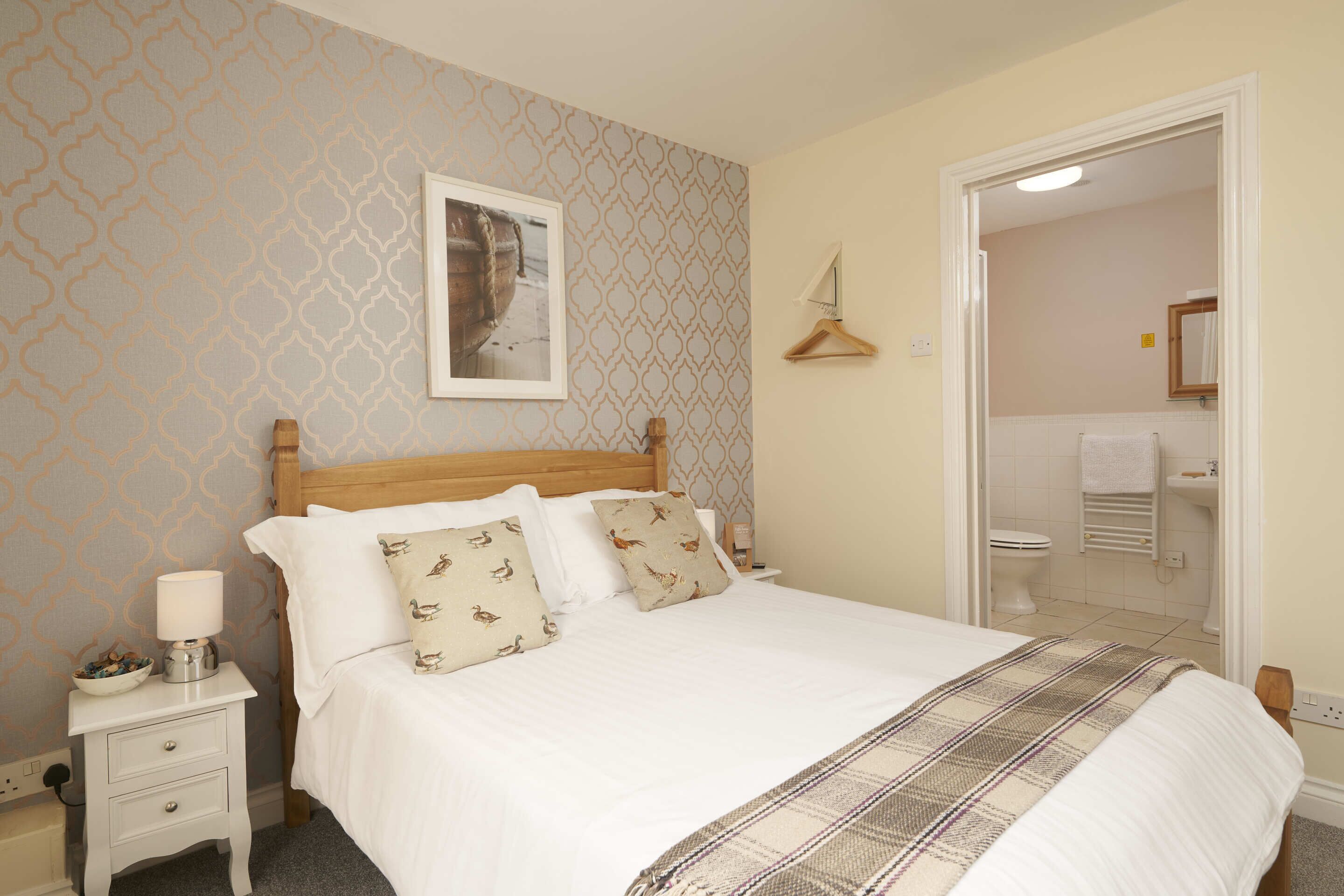 A neatly made bed with a plaid blanket, a bedside table with a lamp, and a framed picture on the wall.