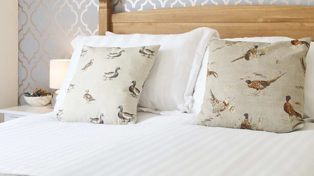 Una cama bien hecha con almohadones estampados, un cabecero de madera y un cuadro enmarcado en la pared.