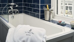 Un baño con baldosas azul oscuro, una bañera blanca, una toalla colgando de un lateral y una ventana con vistas al exterior.