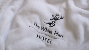 Una bata blanca con texto bordado y el logo de un ciervo, que indica que pertenece al Hotel White Hart.