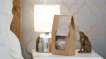 Una mesita de noche con una lámpara, una bolsa de papel marrón etiquetada “Fifth Sense Overnight Spa Kit” y una pequeña estatua dorada.