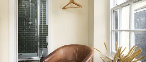 A bathroom with a shower, a brown leather chair, and a window with a view of a building.