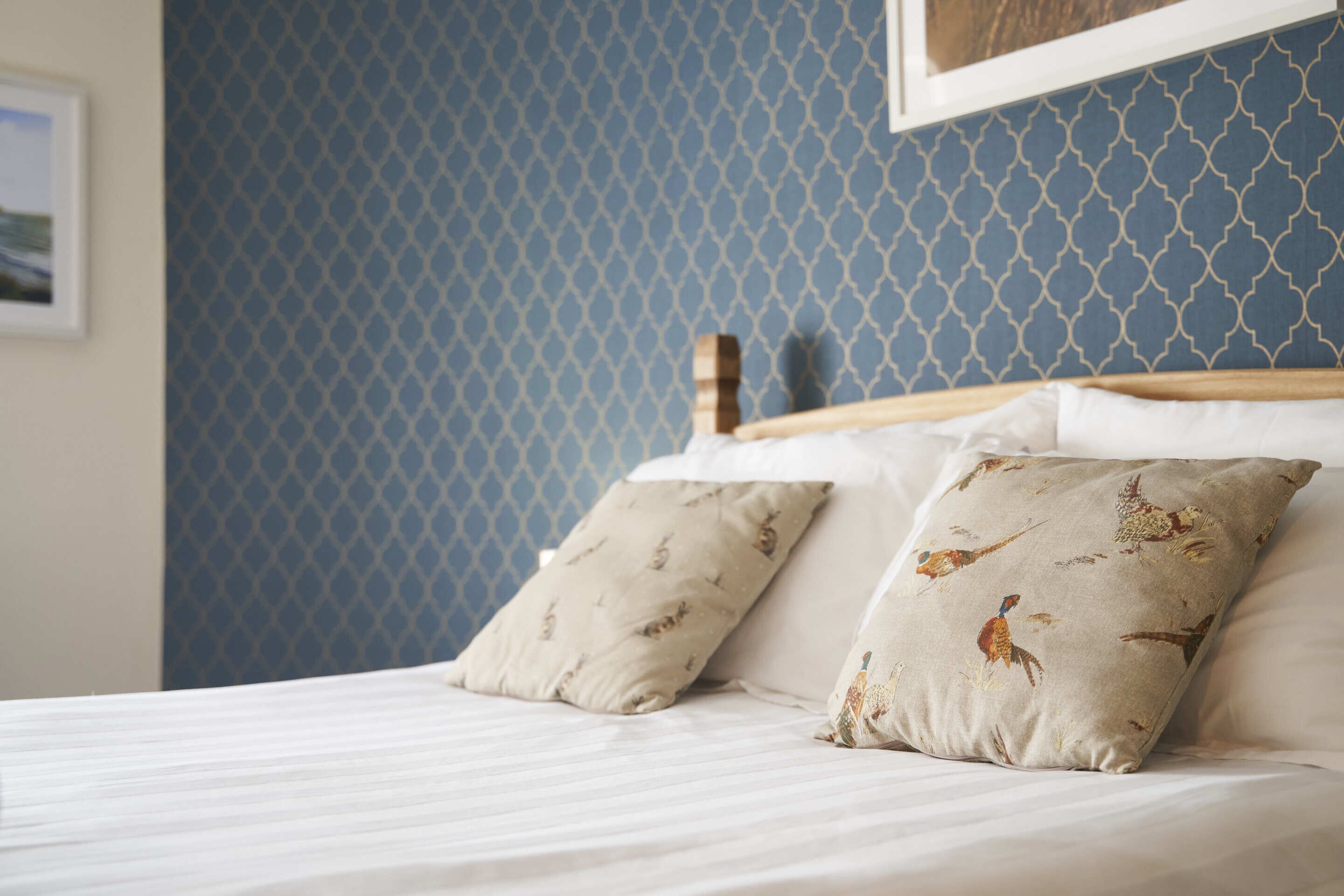 A bed with two pillows, a wooden headboard, and a blue patterned wall.