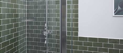 A bathroom with a glass-enclosed shower, a white toilet, and green-tiled walls.