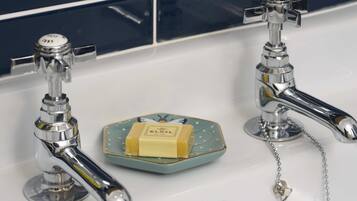 Two chrome faucets on a white sink with a soap bar on a decorative dish.