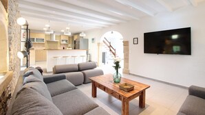 Een moderne woonkamer met een bank, een houten salontafel en een flatscreen-tv aan de muur.