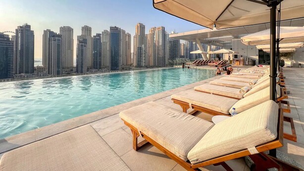 Une piscine sur le toit, dotée de chaises longues et de parasols, offrant une vue panoramique sur la ville.