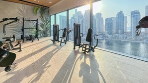 Une salle de sport équipée de matériel d’exercice et dotée d’une grande fenêtre donnant sur un paysage urbain.