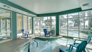An indoor swimming pool with clear glass walls, blue chairs, and a view of palm trees and a poolside area. - Gulfport Oceanfront Vacation Rental: Walk to Beach (Gulfport)