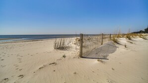 A sandy beach with footprints leading to a striped gate, overlooking the ocean. - Gulfport Oceanfront Vacation Rental: Walk to Beach (Gulfport)