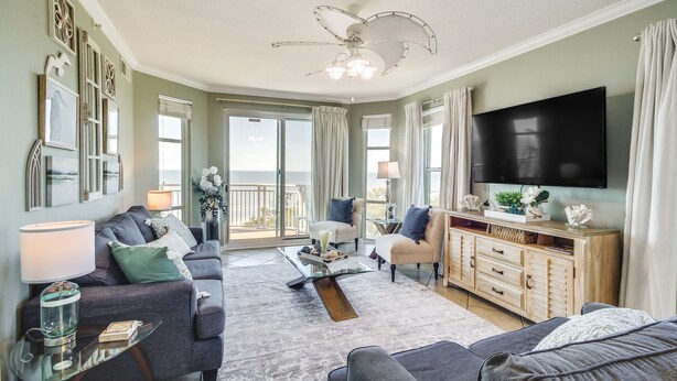 A spacious living room with a ceiling fan, a flat-screen TV, and a large window offering a view of the outdoors. - Gulfport Oceanfront Vacation Rental: Walk to Beach (Gulfport)