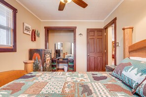 A bedroom with a large bed, a wooden headboard, a ceiling fan, a dresser with drawers, a mirror, and a door leading to another room.