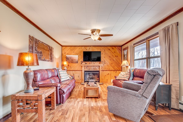 A cozy living room with a fireplace, leather sofas, a wooden coffee table, and a ceiling fan.