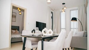 A modern dining area with a table set for two, white chairs, and pendant lighting. - Green community 1BR 15 min to sea (Dubai)