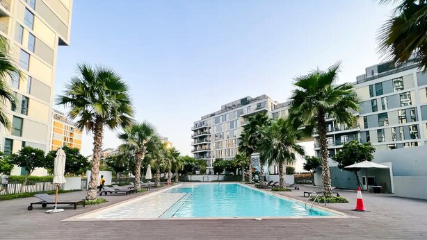 A swimming pool surrounded by palm trees and modern buildings. - Green community 1BR 15 min to sea (Dubai)