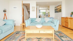 Una sala de estar con un sofá azul claro, una mesa de centro de madera con un cuenco y una alfombra estampada.