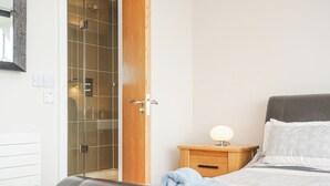 Un dormitorio con cama, mesita de noche, puerta de madera y baño con cabina de ducha de vidrio.