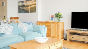Una sala de estar moderna con un sofá azul claro, una mesa de centro de madera y un televisor de pantalla plana sobre un mueble de madera.