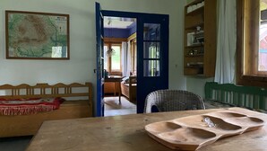 Ein Zimmer mit einem hölzernen Bett, einem Esstisch, einem Korbstuhl, einer Karte an der Wand und einer blauen Tür, die in einen anderen Raum führt.