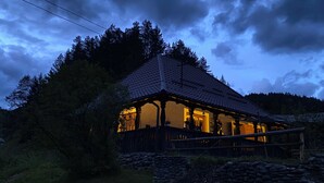 Ein rustikales Blockhaus mit Ziegeldach, umgeben von Bäumen und einer Steinmauer.