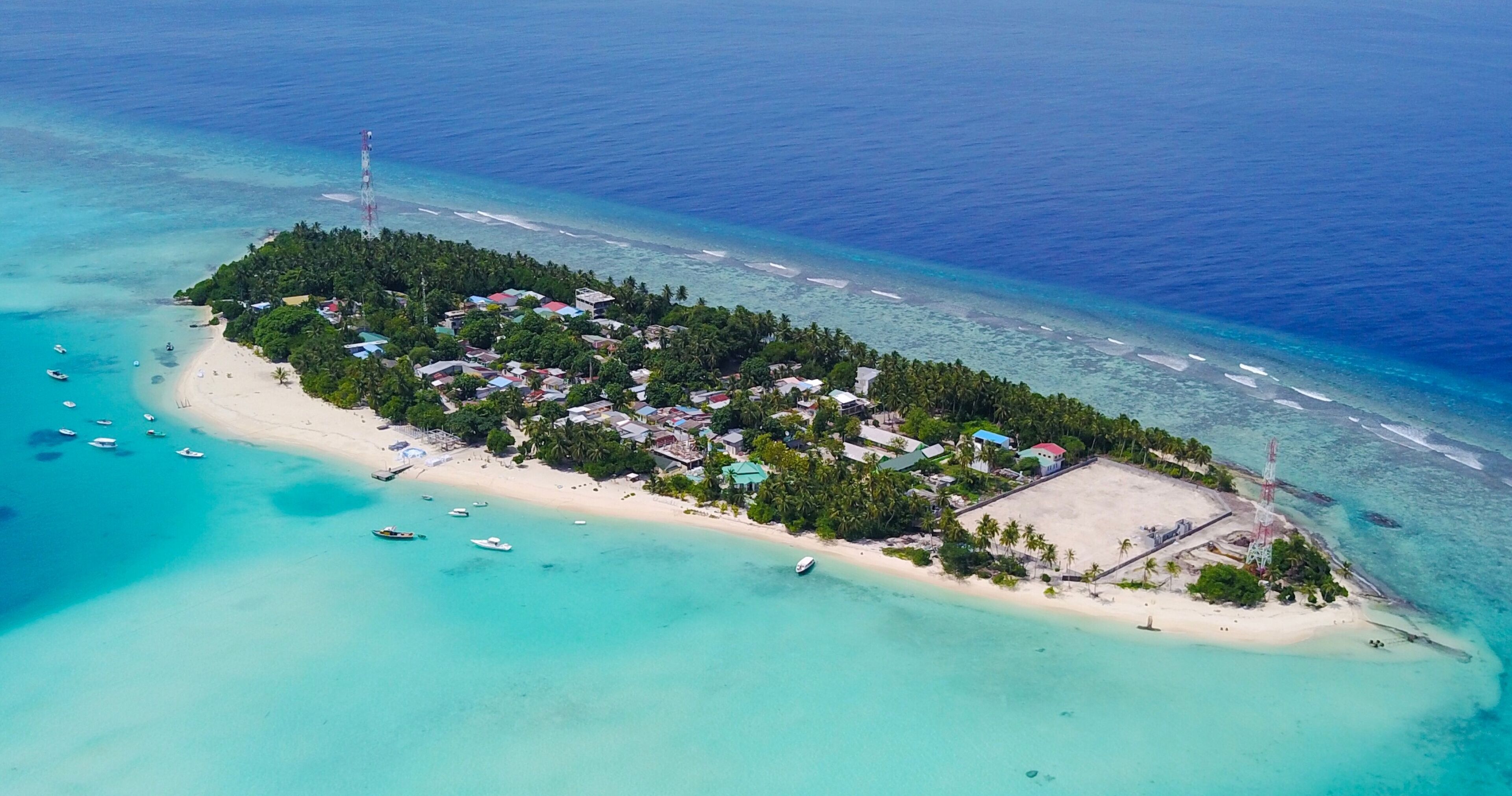 An aerial view of a tropical island with a beach, boats, and buildings.