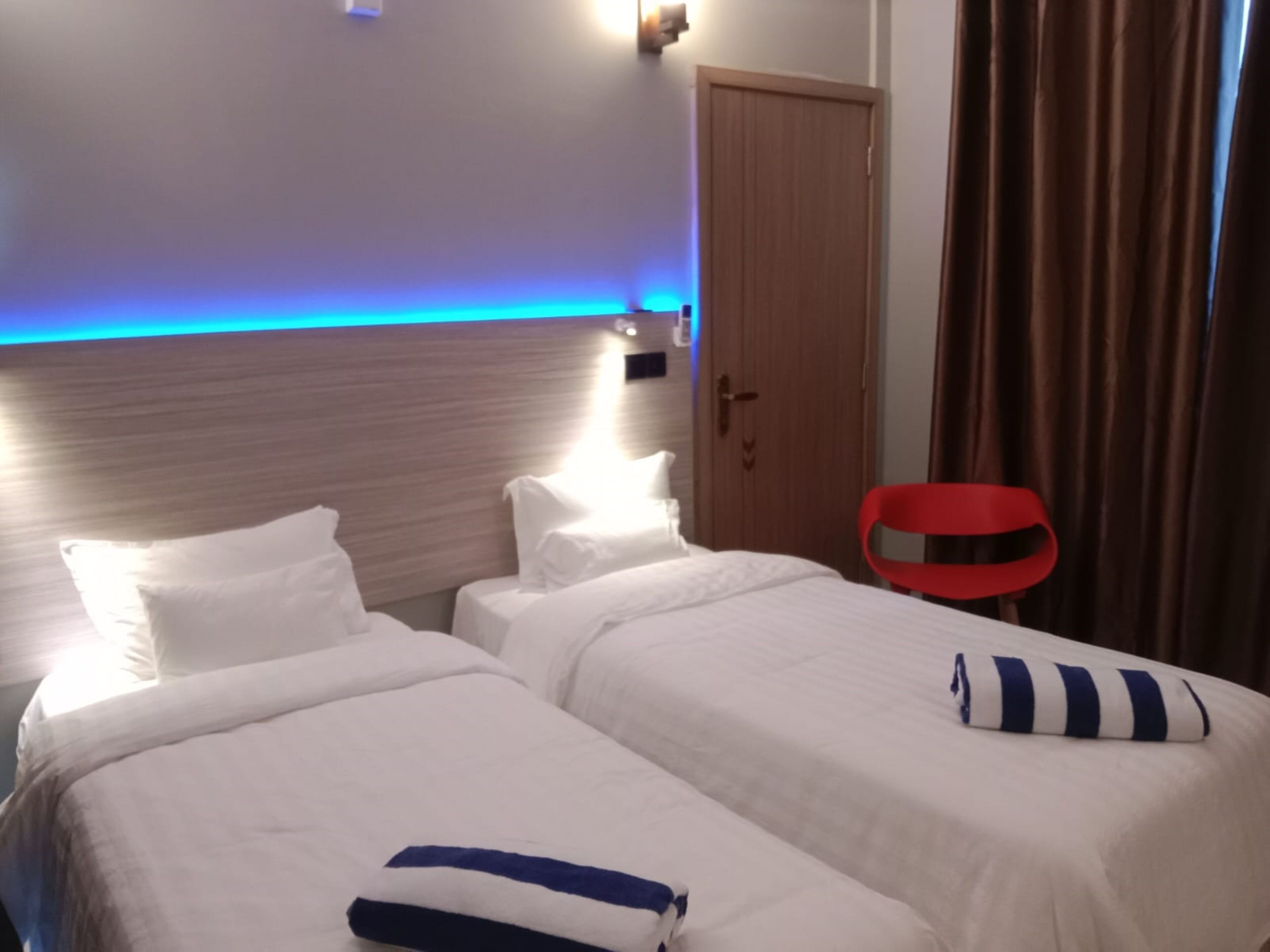 A hotel room with two beds, a wooden headboard, a red chair, and a door.