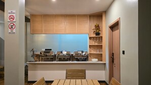 A modern kitchen with wooden cabinets, a built-in stove, and a dining area with a wooden table and chairs. - Madi Grand Maldives  (Fulidhoo)
