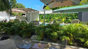 A poolside area with outdoor seating, umbrellas, and lush greenery. - Madi Grand Maldives  (Fulidhoo)