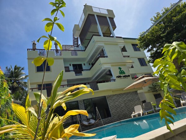 A multi-story building with a pool area, including lounge chairs and a water feature. - Madi Grand Maldives (Fulidhoo)