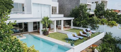 A modern house with a swimming pool, outdoor seating, and lush greenery.